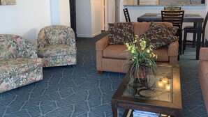 A living room with patterned sofas, a coffee table with a vase, and a view into a kitchen with a dining area. - Cozy oceanfront beach condo full of light (North Myrtle Beach)