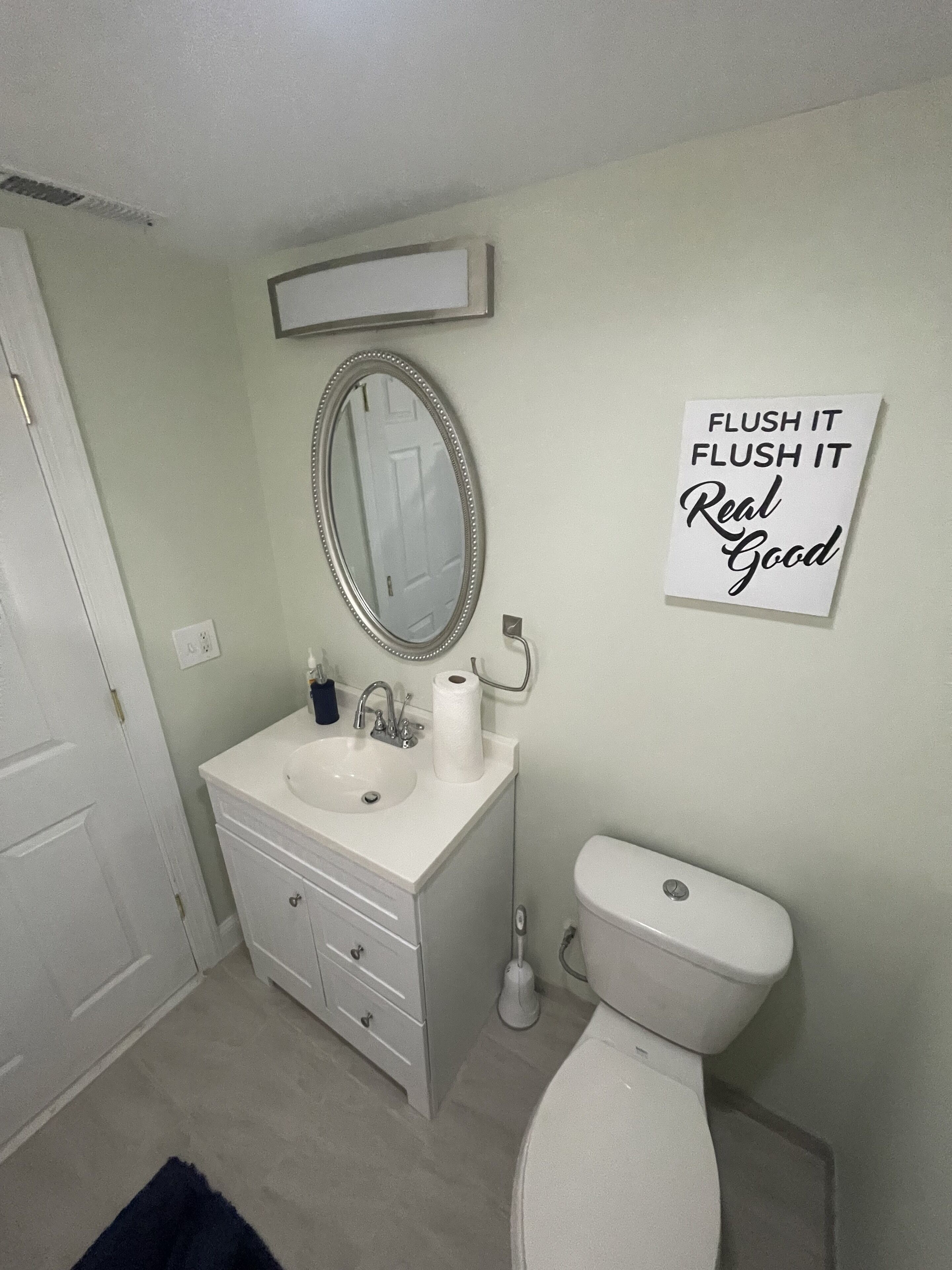 A bathroom with a white sink, mirror, and toilet. A sign on the wall reads "Flush it Flush it Real Good."