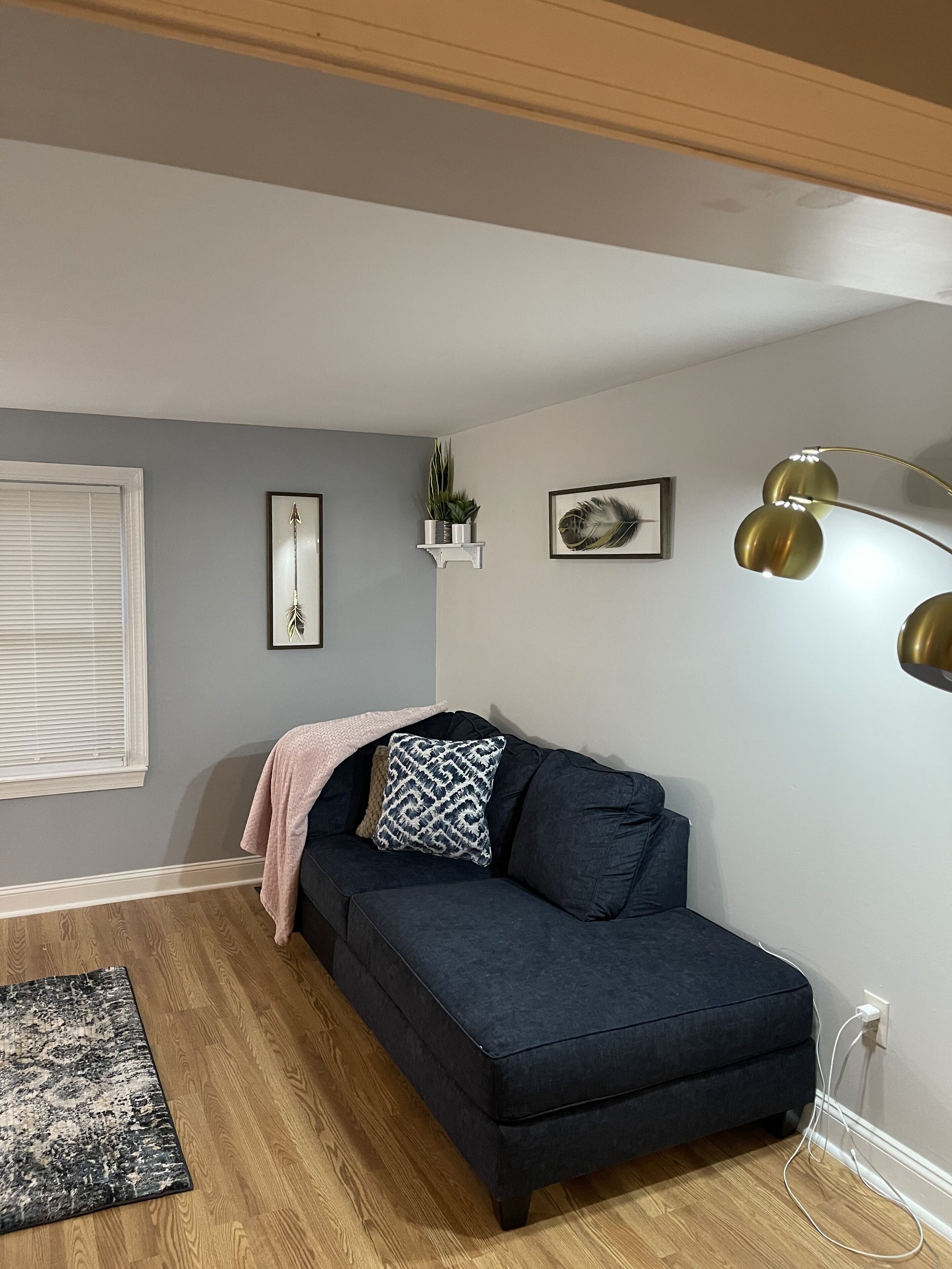 Un salon chaleureux avec un canapé bleu foncé, une petite table d’appoint ornée d’une plante, un tableau encadré et une lampe sur pied.