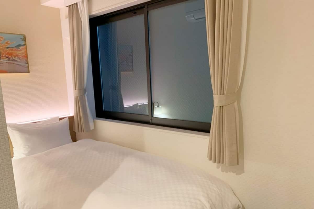 Ein Hotelzimmer mit Bett, einem Fenster mit Vorhängen und einem Bild an der Wand.