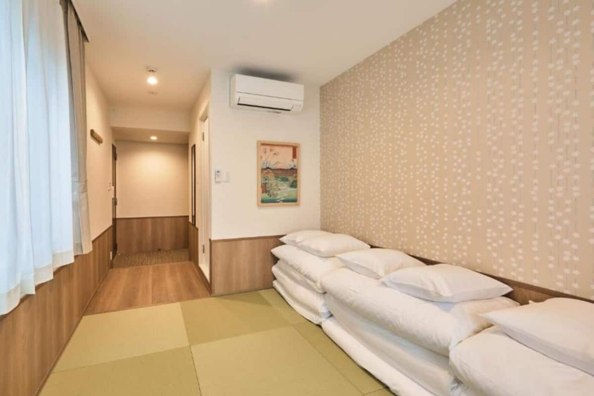 Ein Hotelzimmer mit Holzboden, einem großen Bett mit weißer Bettwäsche, einer Klimaanlage, einem Gemälde an der Wand und Tapete mit Muster.