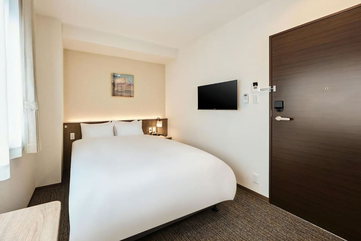 Ein Hotelzimmer mit einem großen Bett, einem flachbildfernseher an der Wand, einer Tür mit Griff und einem kleinen Tisch.