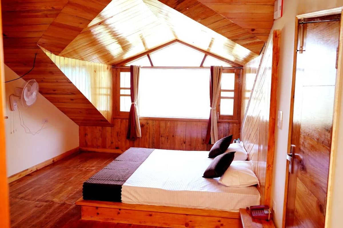 A cozy bedroom with a sloped ceiling, wooden walls, a bed with pillows, and a window with curtains.