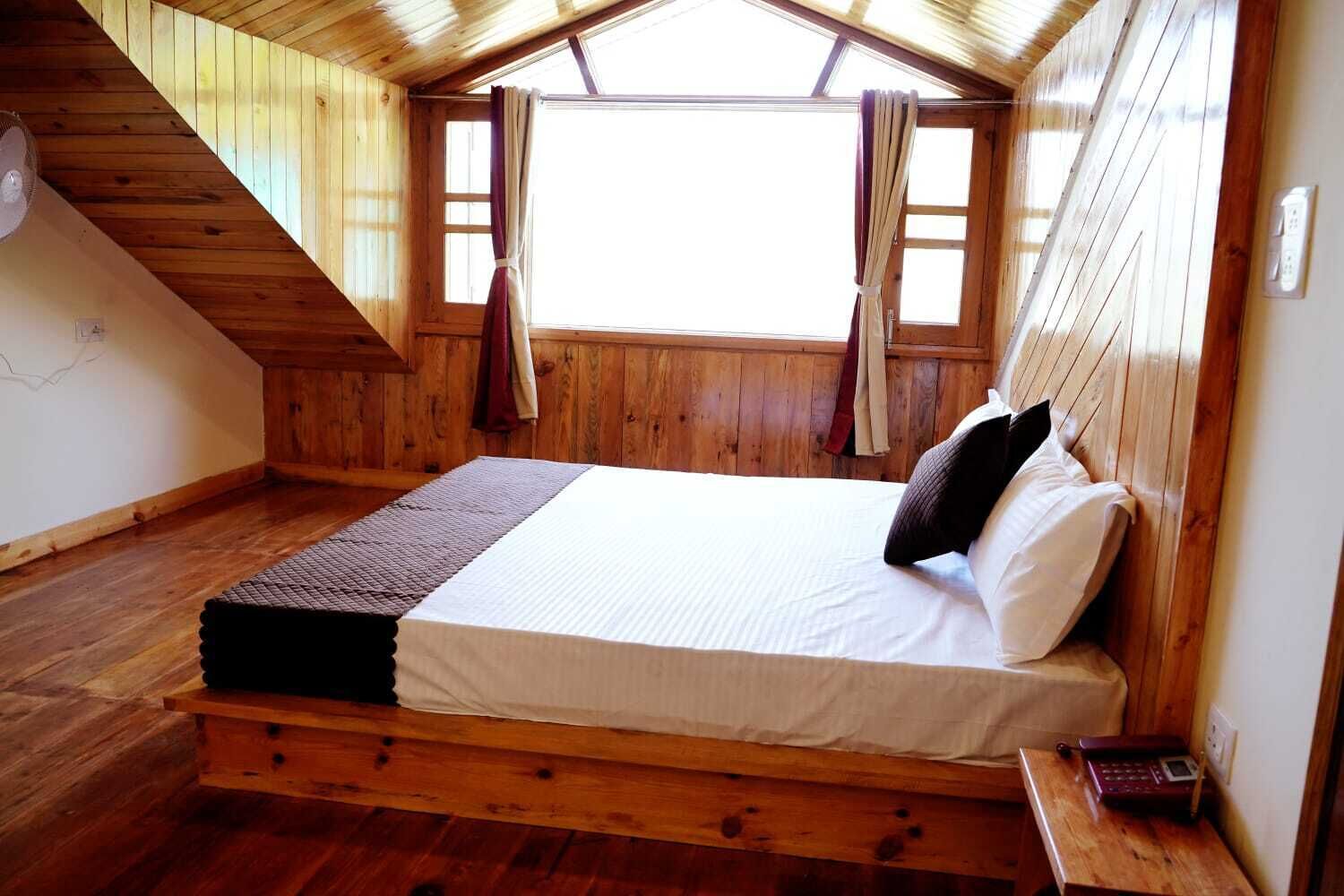 Un dormitorio de cabaña de madera con una cama, una mesita, un calentador y una ventana con cortinas.