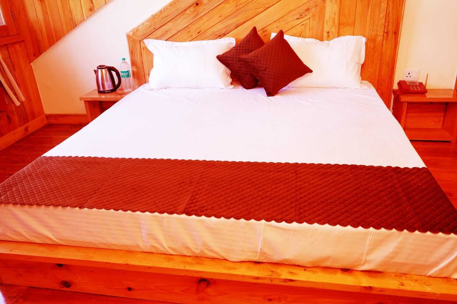 A wooden-framed bed with white bedding and a brown quilt.