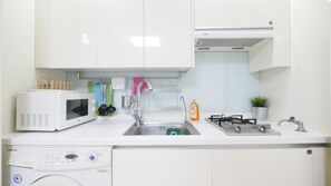 A modern kitchen with white cabinetry, a microwave, a dishwasher, a sink with a faucet, a stove, and a small potted plant.