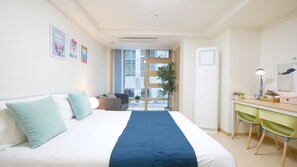A hotel room with a bed, a desk, a chair, a window, and a door.