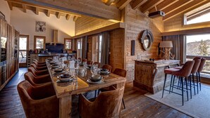 A wooden interior with a long dining table set for six, a kitchen area, and a bar with stools. - Chalet Flocon de Neige - jacuzzi - sauna - La Tzoumaz, 4 Vallees (La Tzoumaz)