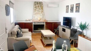 Un salon avec une cheminée, un canapé, un téléviseur et un coin repas comprenant une table et des chaises.