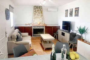 A living room with a fireplace, sofa, TV, and a dining area with a table and chairs.