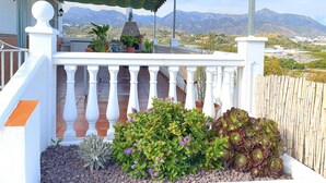 Un balcon avec vue sur les montagnes, agrémenté de plantes en pot et surmonté d’un auvent rayé.