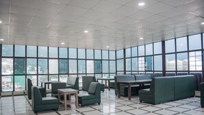 Un espacio interior amplio con ventanas grandes, asientos verdes y piso de baldosas.