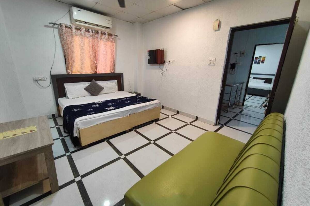Quarto com cama, um banquinho, ventilador de teto, ar condicionado e porta que dá para outro cômodo.