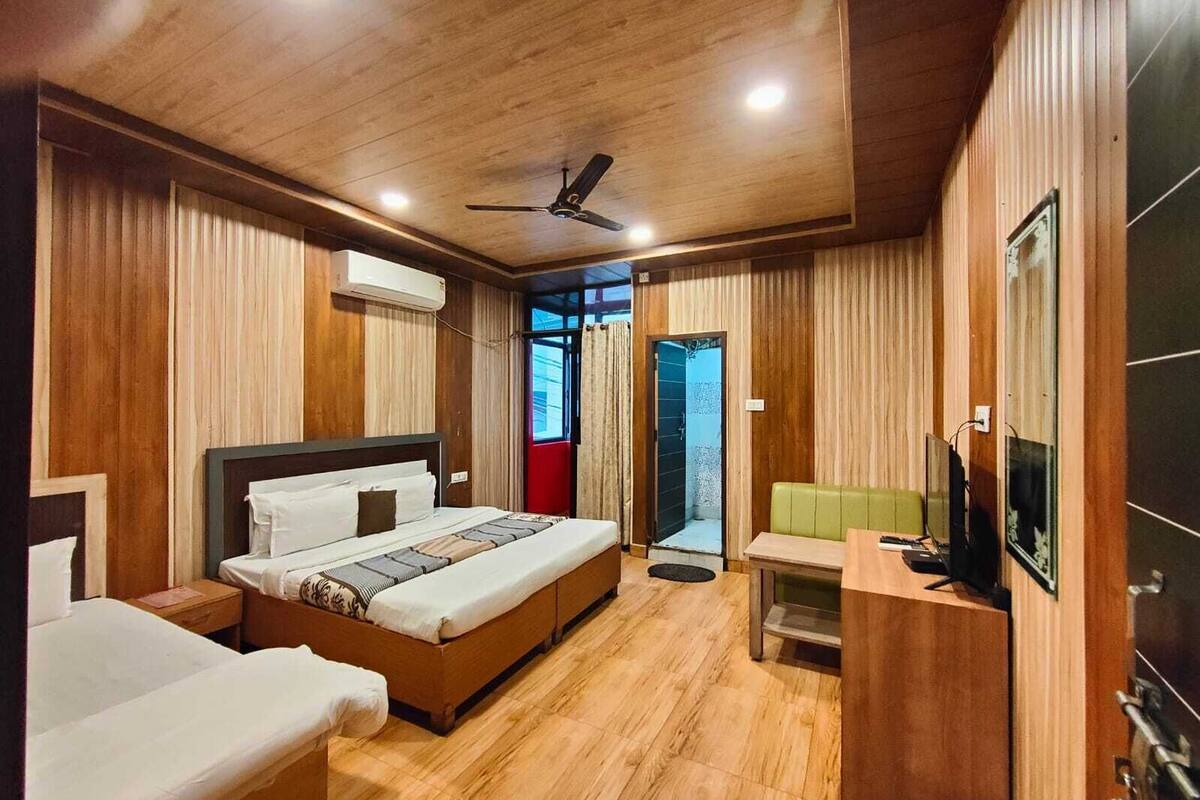 Quarto de hotel com teto de madeira, cama com cabeceira, escrivaninha com cadeira e televisão.