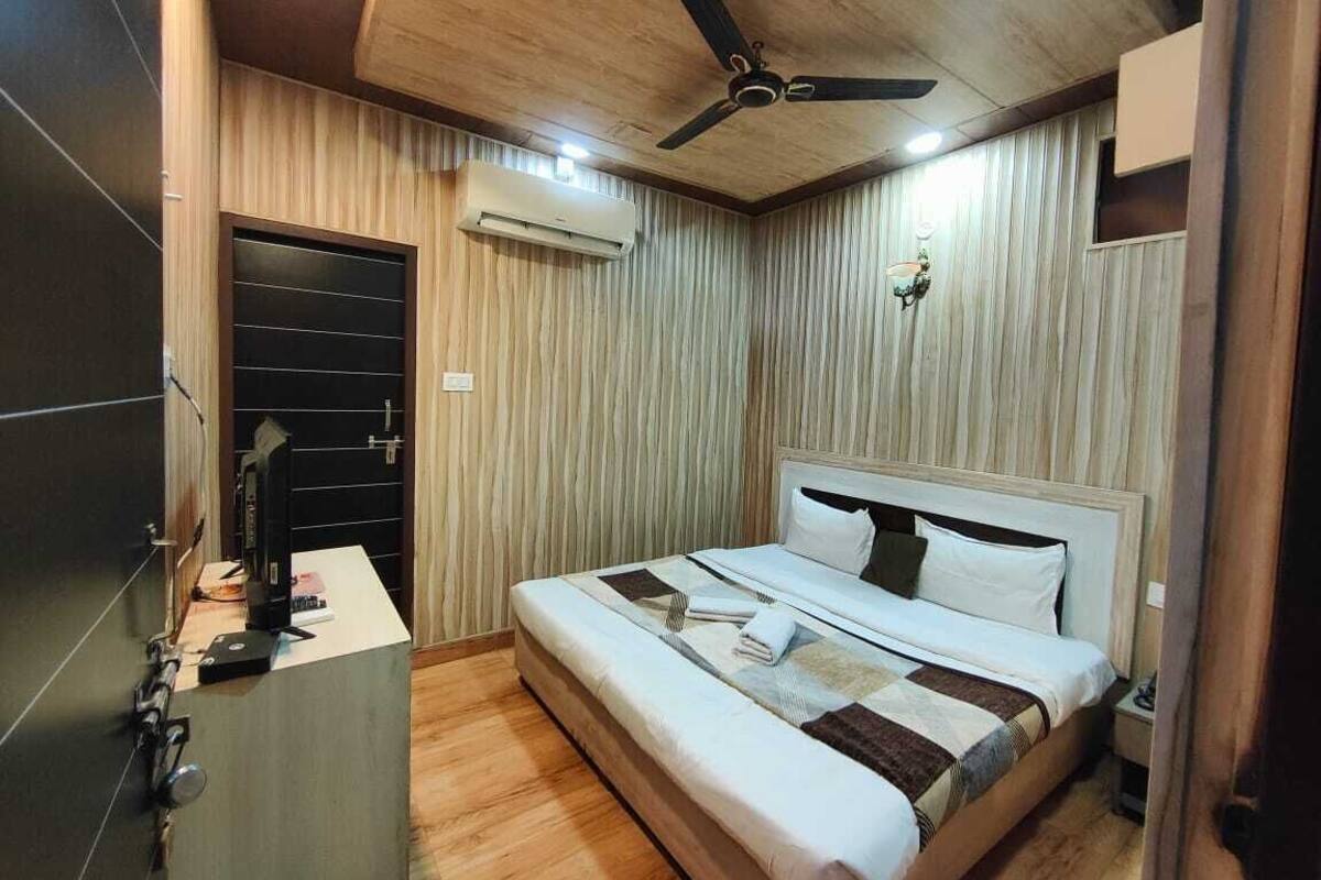 Quarto com cama, ventilador de teto, ar condicionado, mesa de cabeceira e porta.