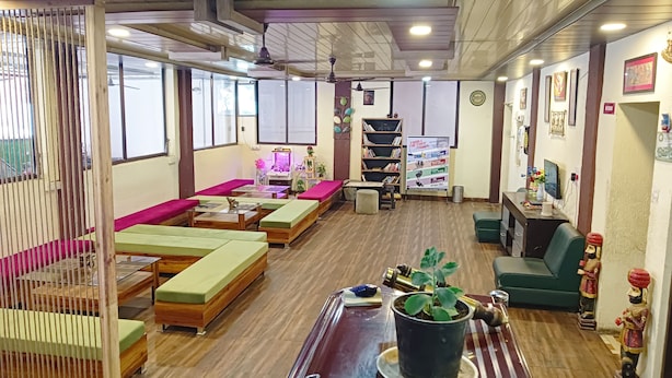 Une pièce avec un plancher en bois, des sièges rembourrés de couleur verte et rose, une table basse en bois, une bibliothèque, une petite table avec une plante et un téléviseur posé sur un bureau.