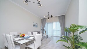 A modern dining area with a white table set for four, a chandelier, and a view of a living room through a glass door. - Chic Marina View Living in a Two Bedroom (Dubai)