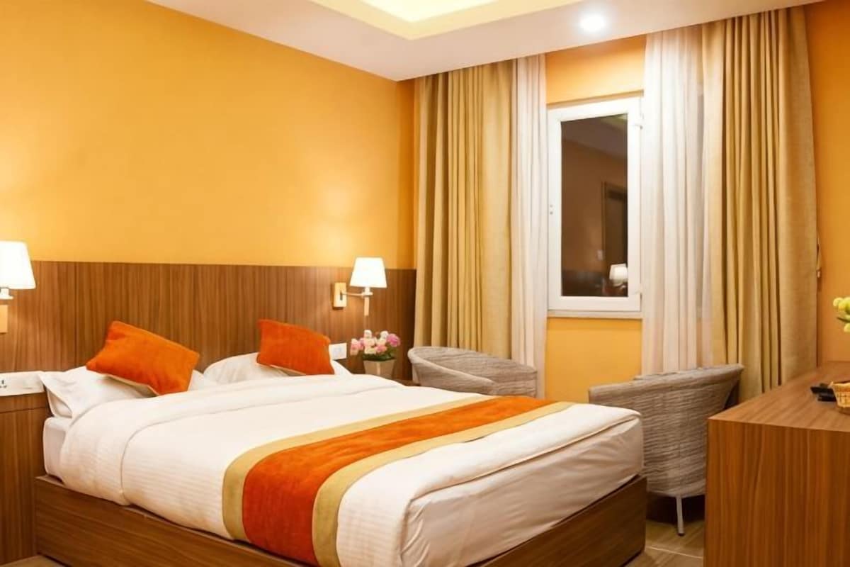 A hotel room with a large bed, two bedside tables, a chair, a desk, and a window with curtains.