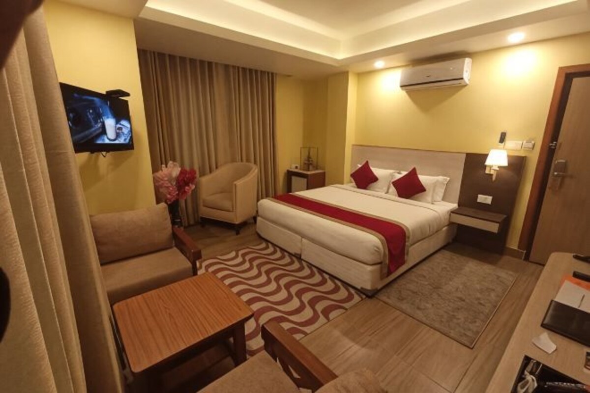 A hotel room with a bed, a sofa, a desk, a TV, and an air conditioning unit.