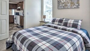 A bedroom with a large bed, a nightstand, a painting on the wall, and a view of the kitchen through an open door. - Blue Mountainview welcomes long stays (Mariposa)