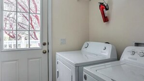 A laundry room with two white washers and dryers, a fire extinguisher, and a window with a view of bare trees. - Blue Mountainview welcomes long stays (Mariposa)