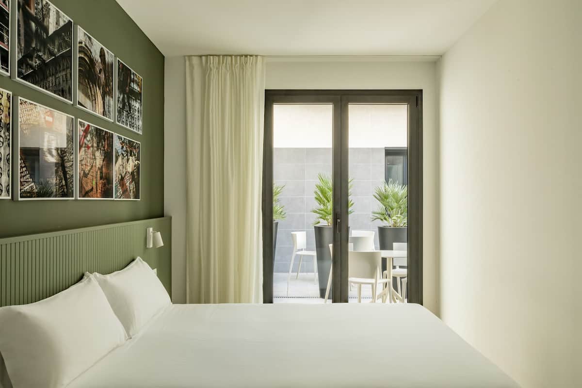 Une chambre d’hôtel avec un grand lit, une vue sur la terrasse extérieure et un mur décoré de tableaux encadrés.