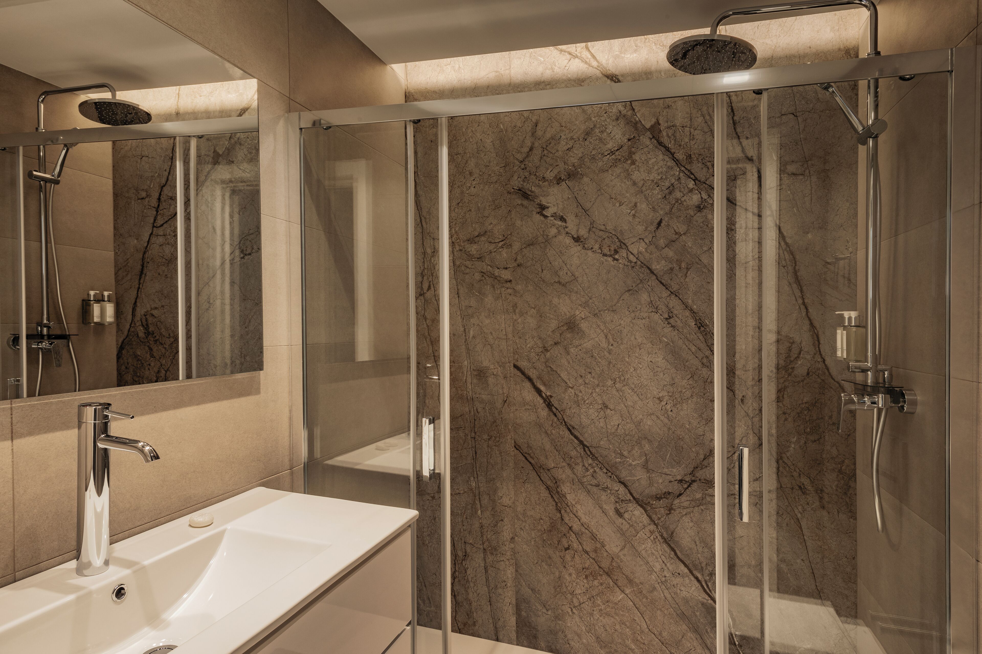 A modern bathroom with a glass-enclosed shower, a white sink, and a marble wall.