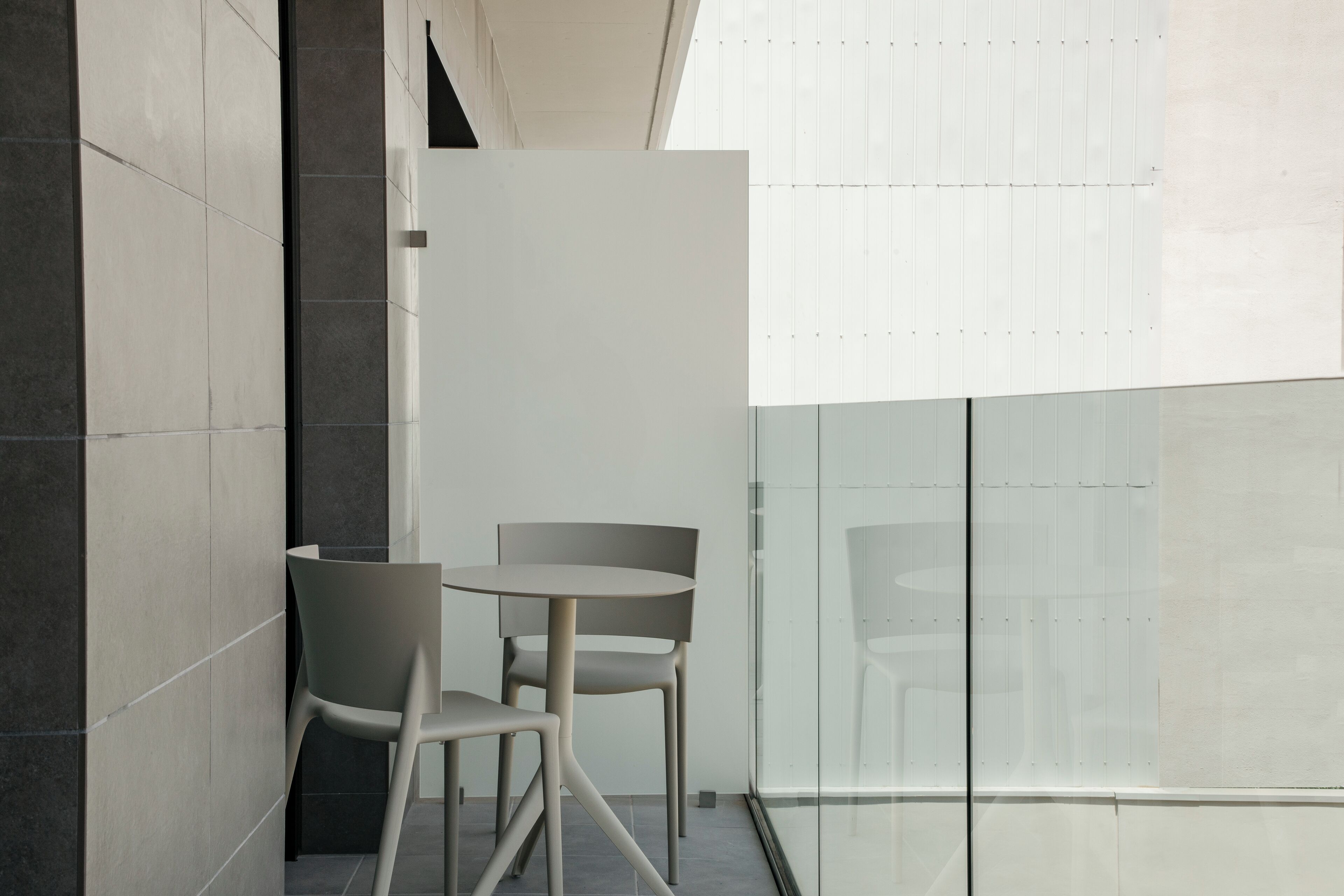 A modern interior with two chairs and a table, a glass partition, and a view of the sky.