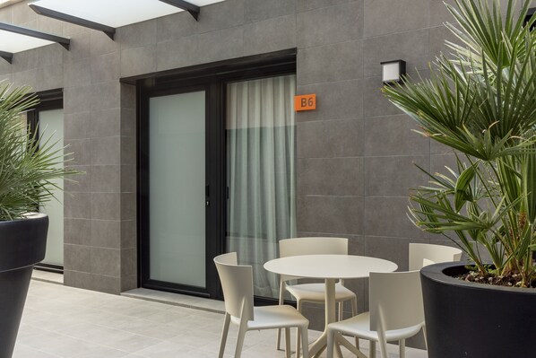 Un espace extérieur moderne, aménagé avec des sièges, une porte d’entrée en verre, un pot de fleurs et un panneau indiquant le numéro de la salle : B6.