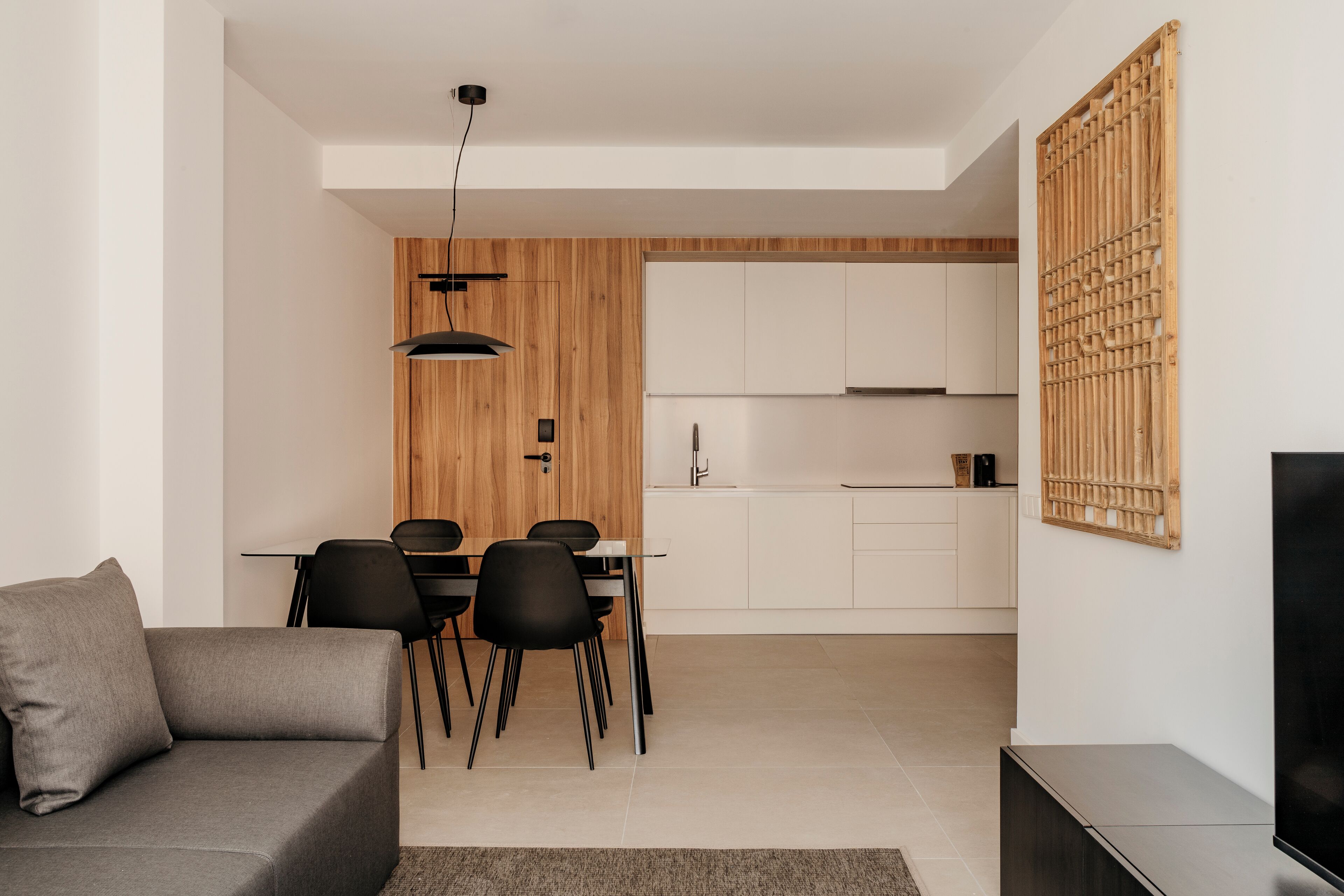 Uma sala de estar moderna com um sofá cinza, uma mesa de jantar com cadeiras, uma cozinha com armários brancos e um rack preto para TV.