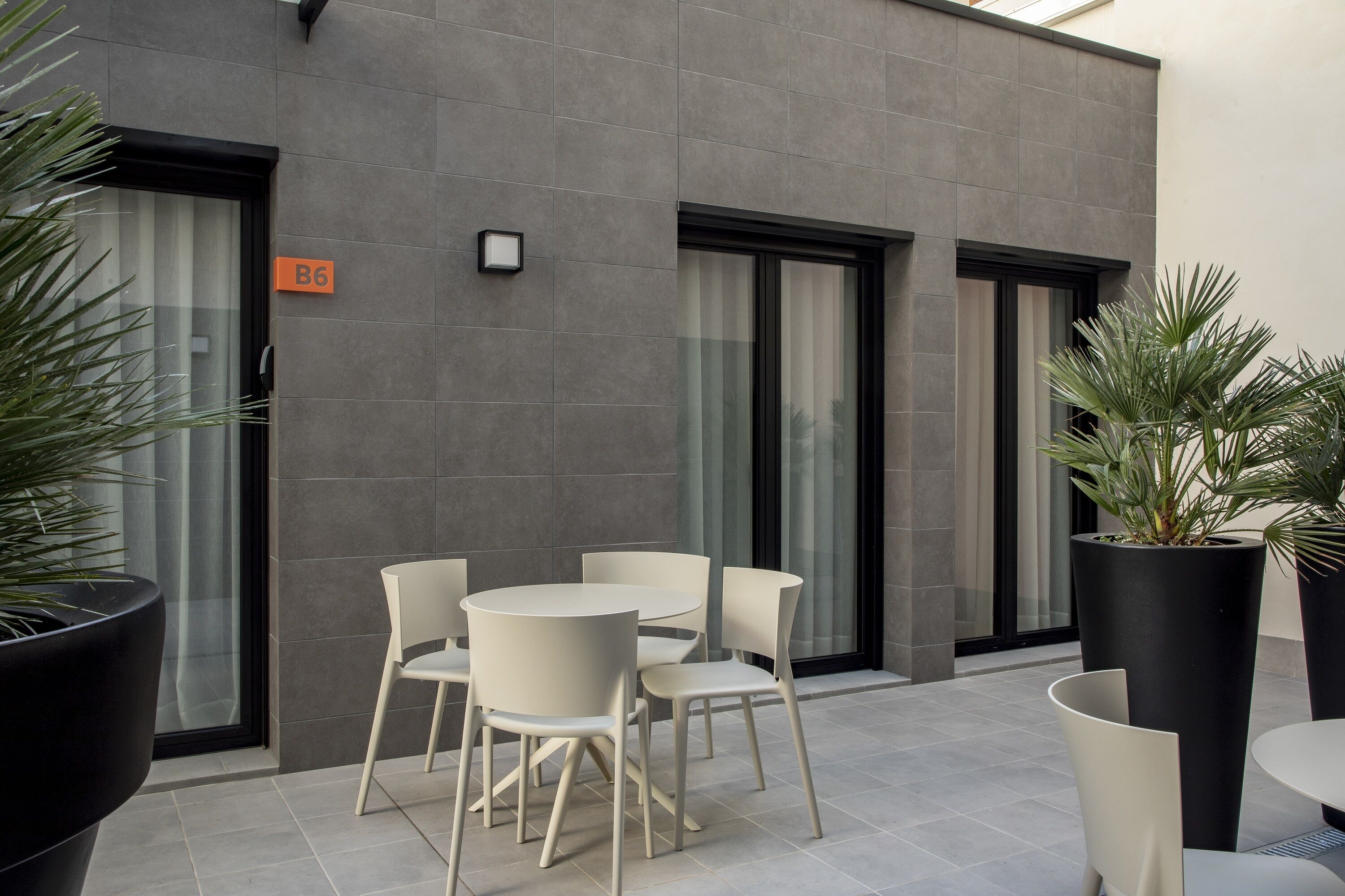 Un espace extérieur moderne aménagé avec une table et des chaises, un pot de fleurs et un bâtiment sur lequel est apposée une enseigne indiquant le numéro de la salle B6.
