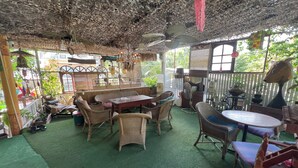 Ein Zimmer mit Decke aus Naturmaterialien, Korbmöbeln und einem grünen Teppich.