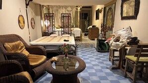A room with a bed, wicker furniture, a glass coffee table, and patterned floor tiles.