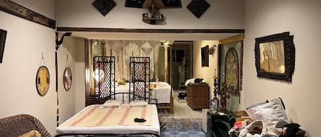 Una habitación con cama, una silla, una mesita y un espejo decorativo.
