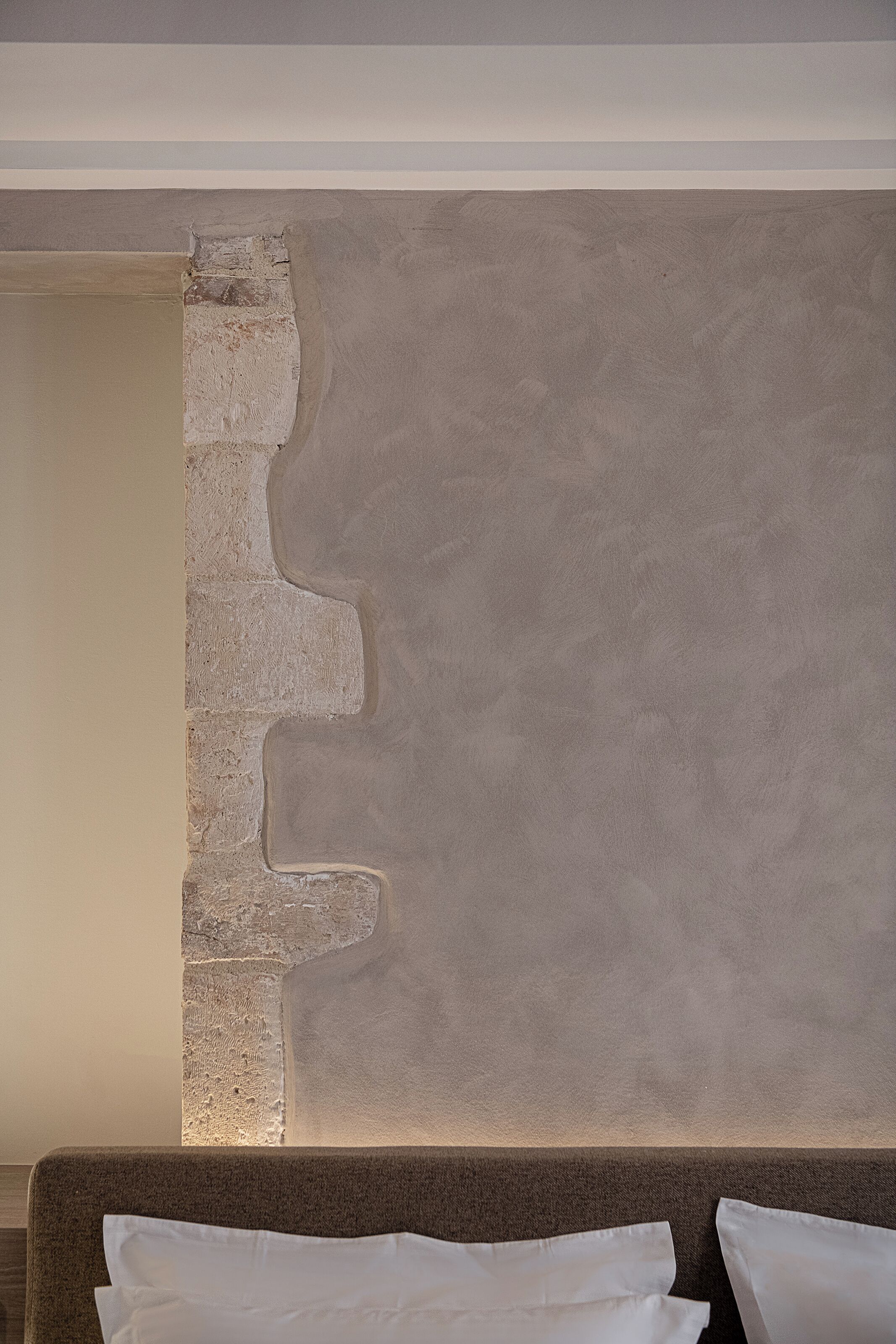 Una habitación con pared texturizada, un sofá con cojines blancos y una esquina visible de la cama.