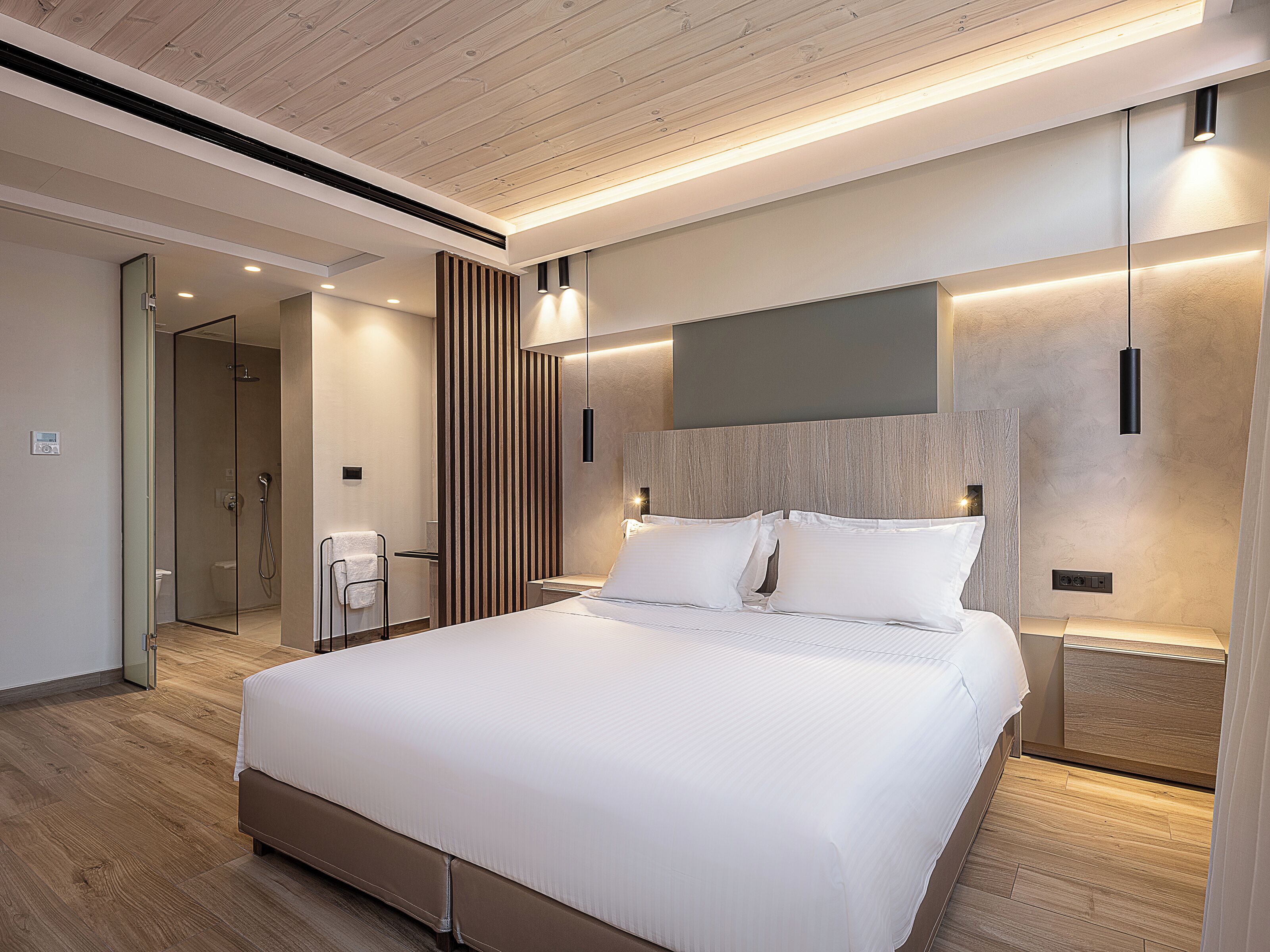 Una habitación de hotel moderna con una cama grande, zona de ducha y techo de madera.
