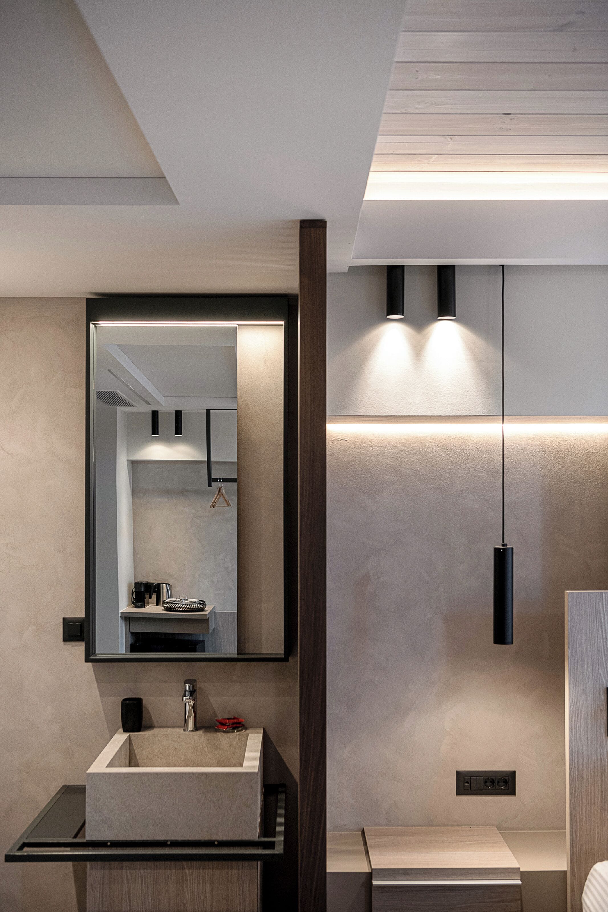 Un baño moderno con un espejo grande, un lavamanos rectangular y una lámpara colgante.