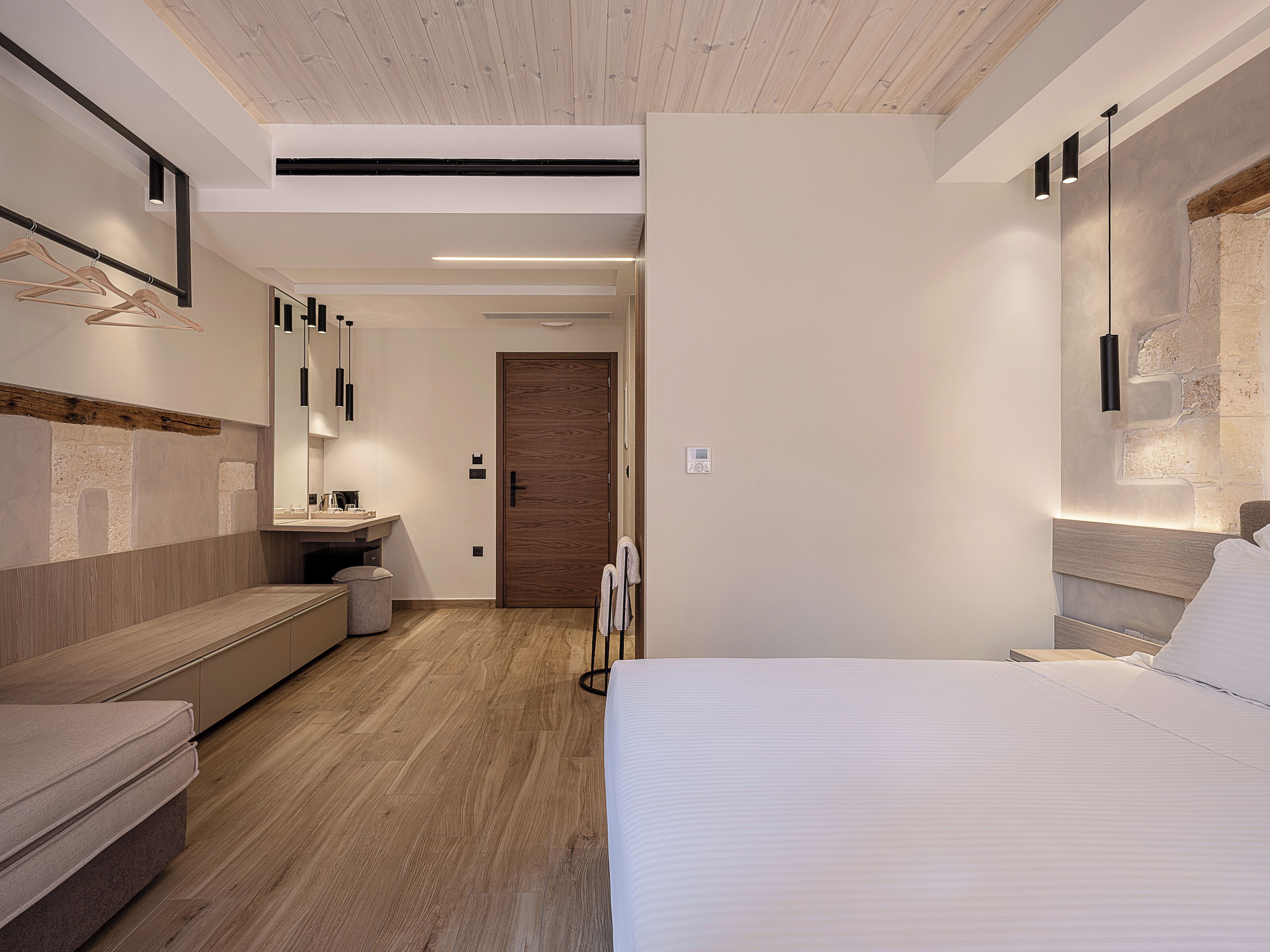 Ein modernes Schlafzimmer mit Holzboden, einem Bett mit weißer Bettwäsche, einem Nachttisch und einer eingebauten Sitzbank.
