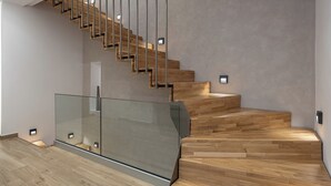 Eine moderne Treppe mit Holzstufen und Glasgeländern, die zu einer oberen Etage führt.
