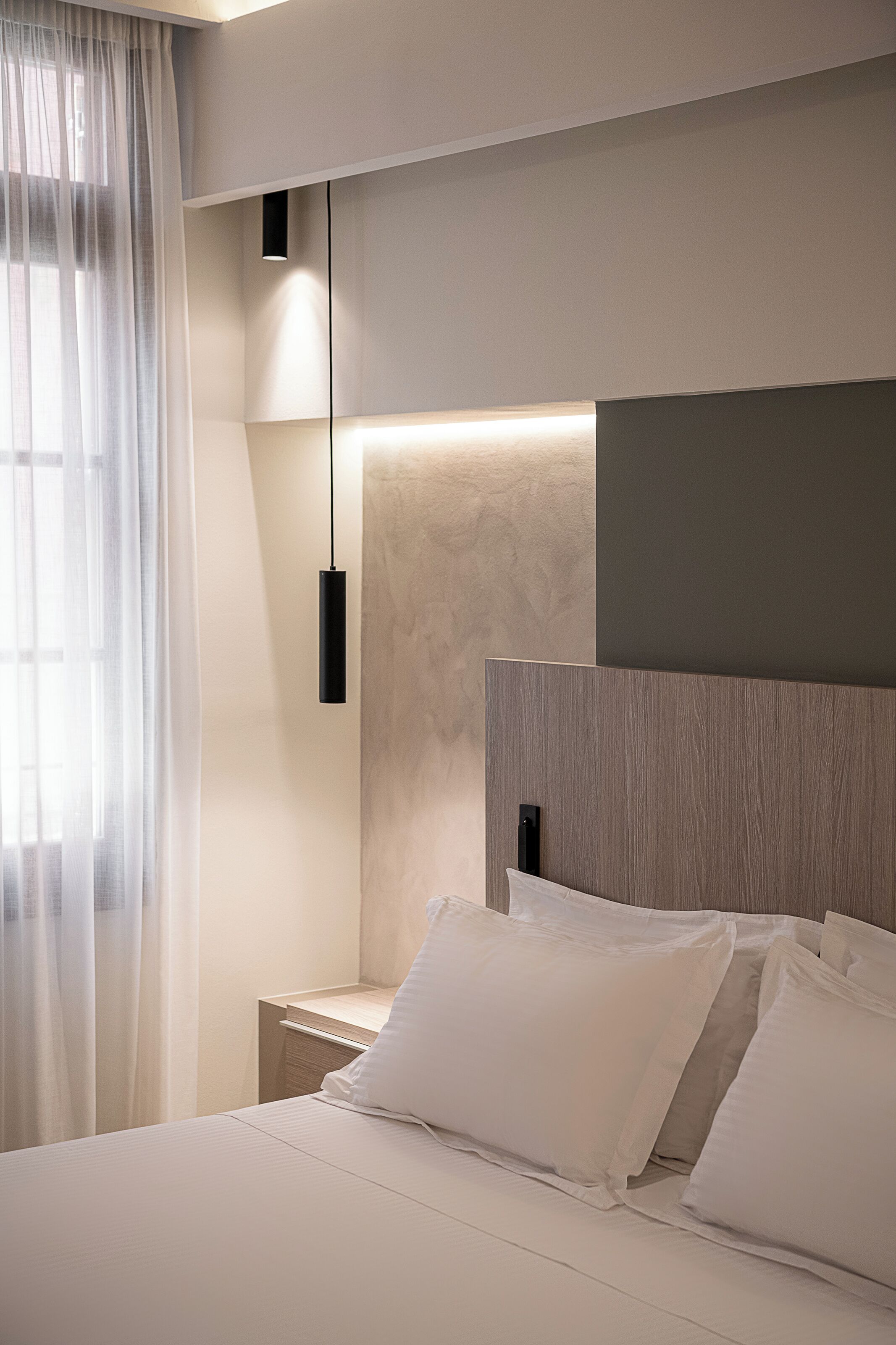 Een moderne slaapkamer met een groot bed, een nachtkastje, een hanglamp en dunne gordijnen.
