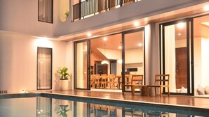 Un área de piscina interior moderna con paredes de vidrio, muebles de madera y un balcón.