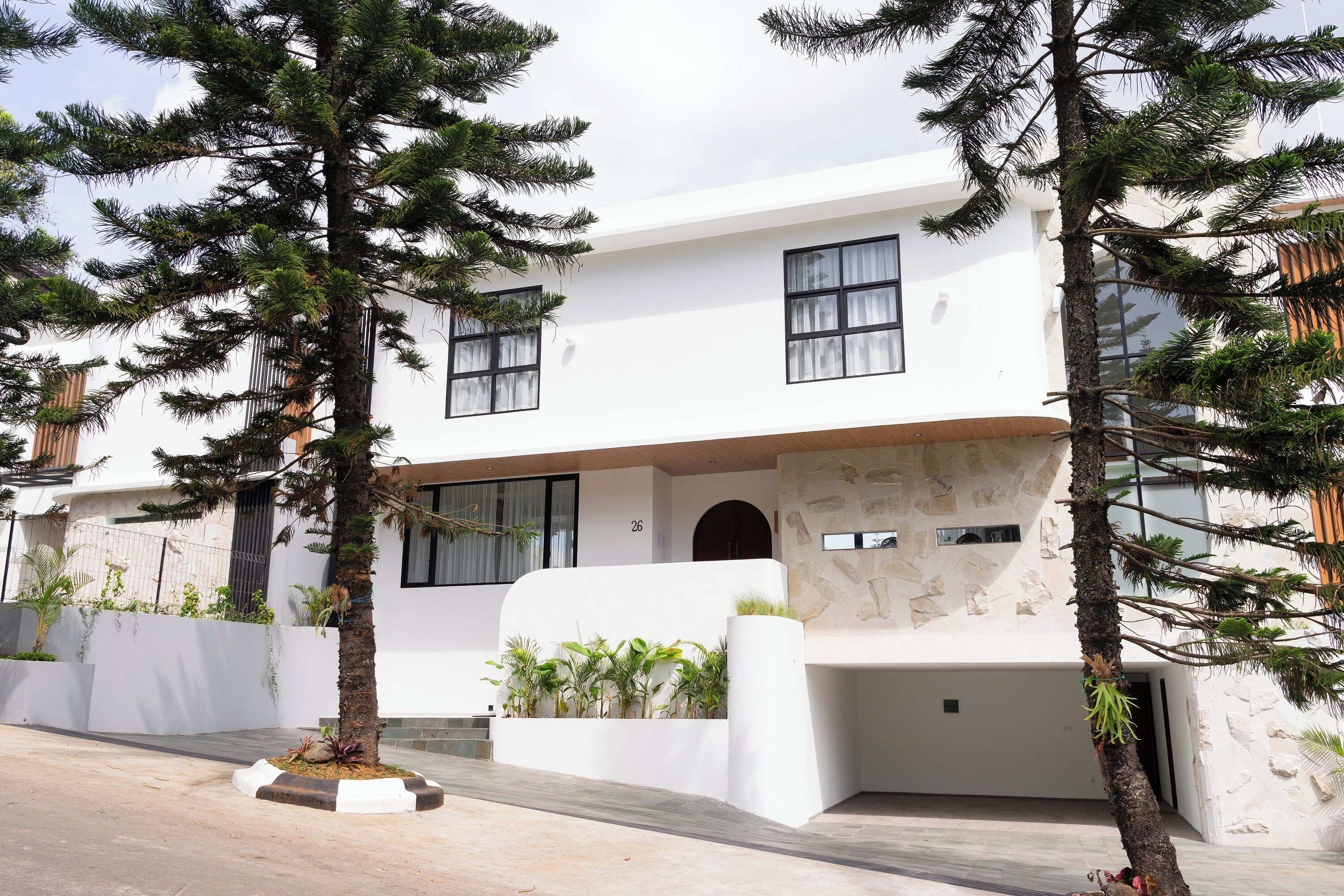 Un edificio moderno de dos plantas con fachada blanca, ventanas amplias y un muro decorativo de piedra.