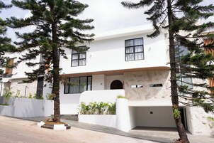 Un edificio moderno de dos plantas con fachada blanca, ventanas amplias y un muro decorativo de piedra.