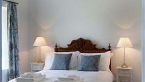 Een opgemaakt bed met witte lakens, twee bedlampjes en een houten hoofdbord.