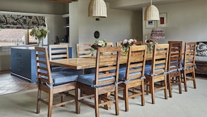 Een eethoek met een houten tafel en stoelen, een keuken op de achtergrond, en hangende rieten lampen.