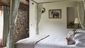 Een slaapkamer met een stenen muur, een bed met bloemenkussens, een schilderij van een olifant en een lamp op een nachtkastje.