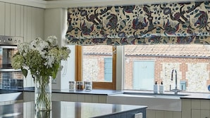 Een keuken met een blauw kookeiland, witte kasten en een decoratief bloemen gordijn boven het raam.