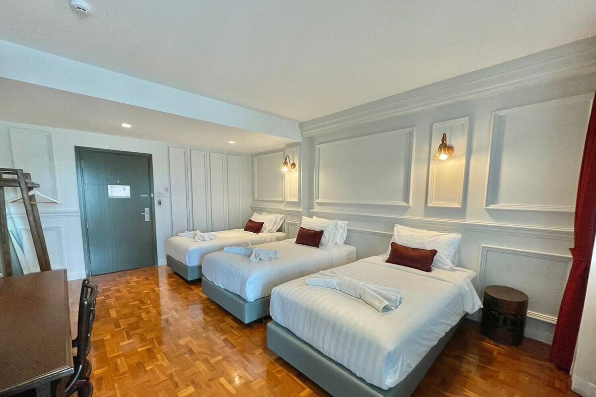 Una habitación de hotel con tres camas, suelo de madera, un escritorio y una puerta.