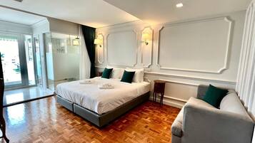 A hotel room with a large bed, a grey armchair, a small table, and a view of the outside through a glass door.