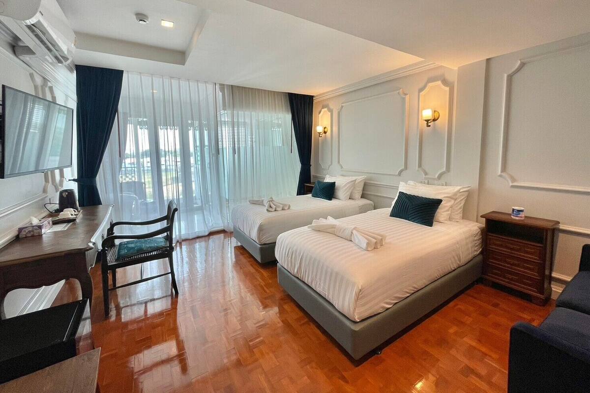 Habitación de hotel con dos camas, un escritorio, una silla, un televisor y una ventana con cortinas.
